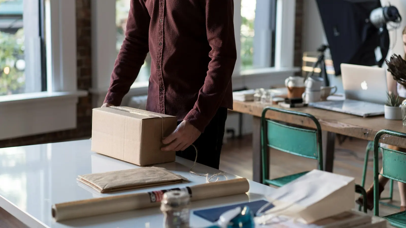 Merchant packing a cardboard parcel on a white table in a bright studio