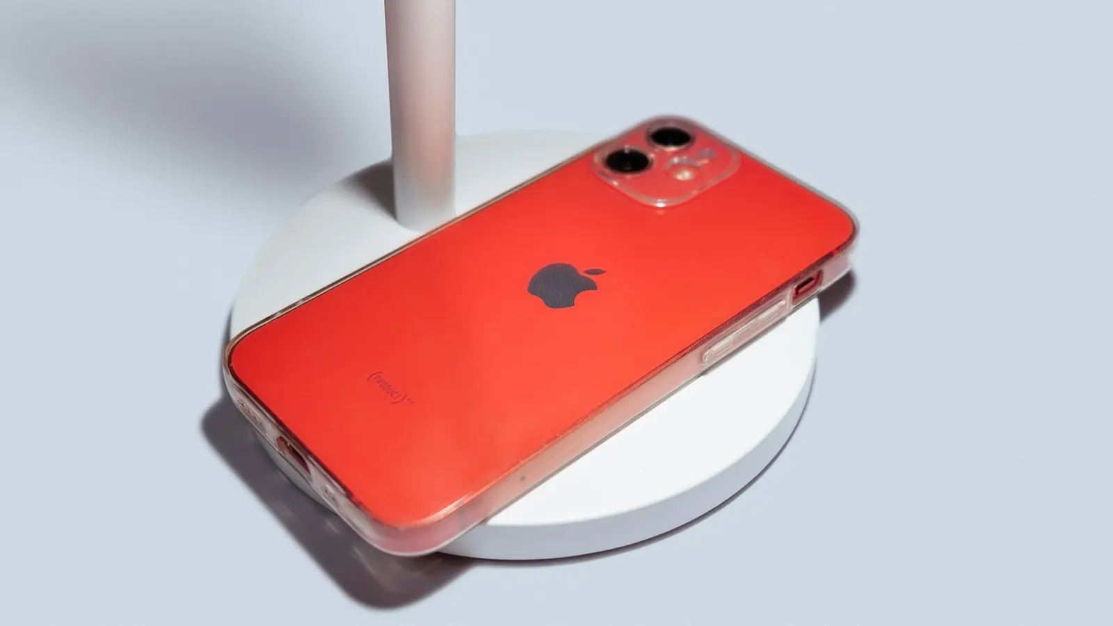 Smartphone rouge posé sur un support blanc, sur fond bleu pâle