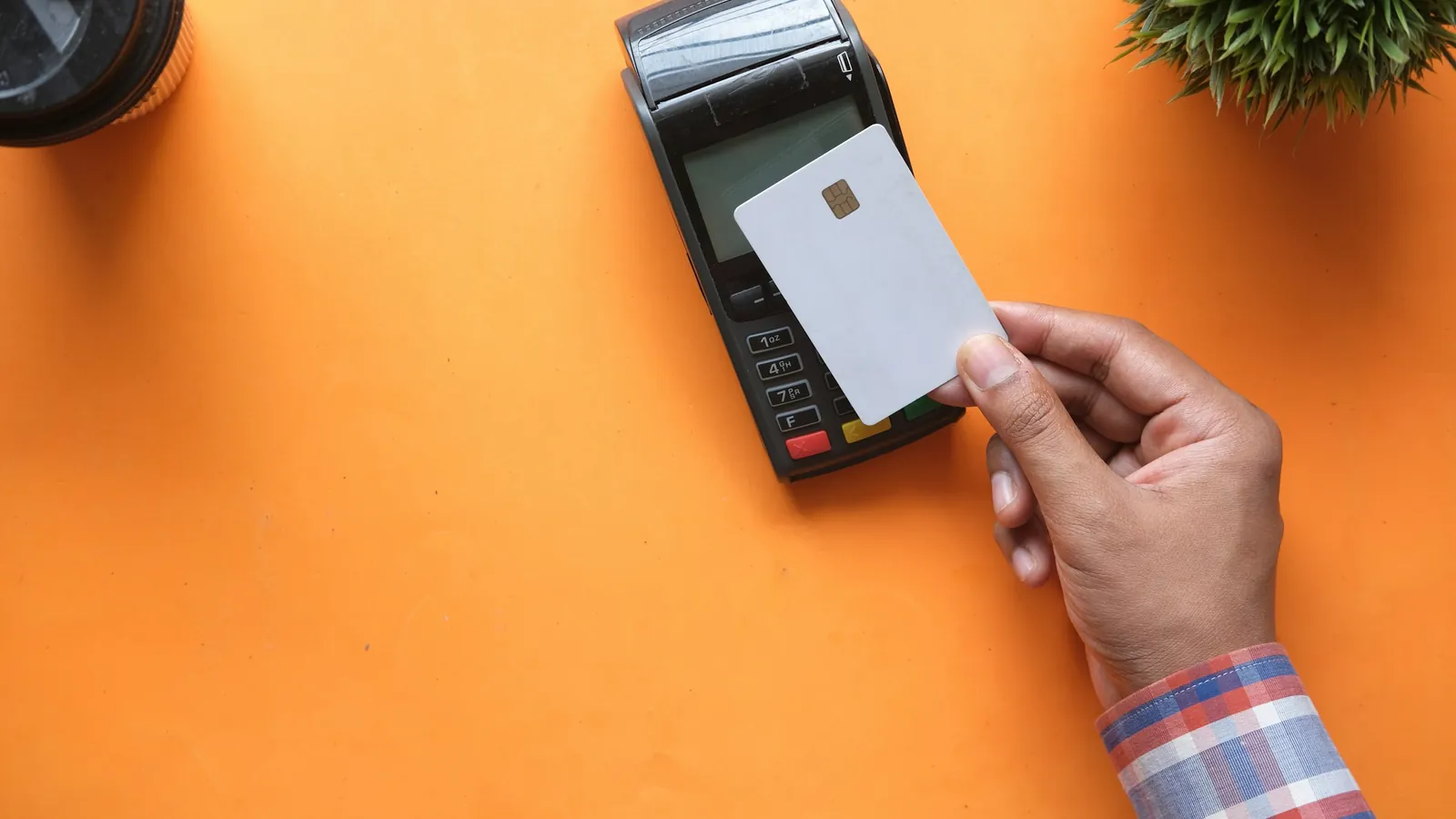 Hand holding a blank white card above a black card terminal on an orange background