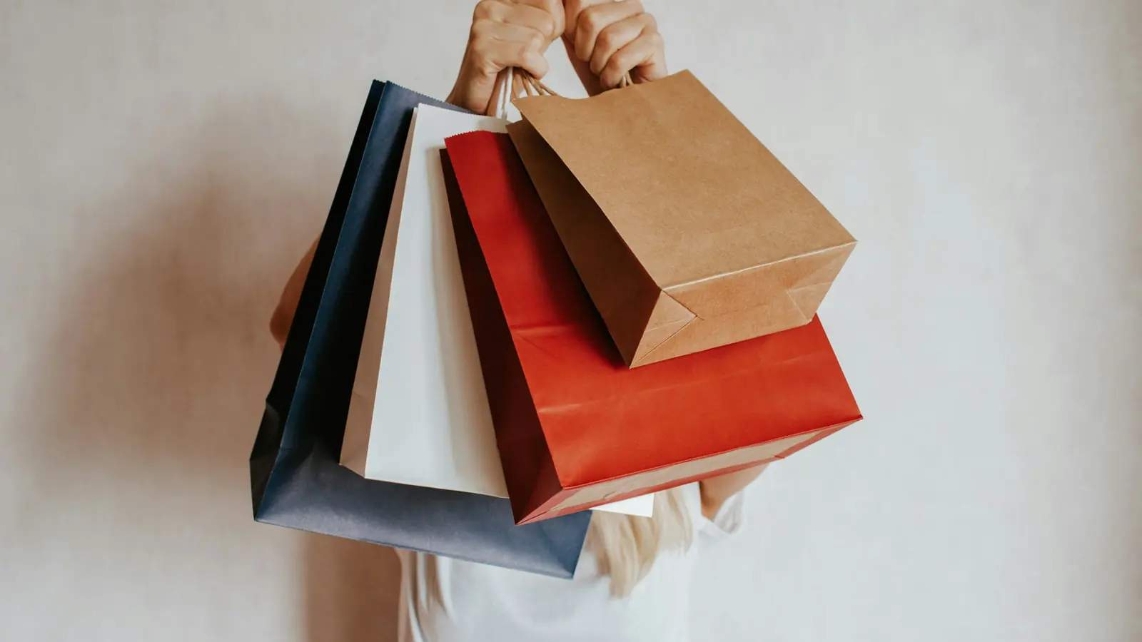 Cliente tenant des sacs de courses rouges, blancs et kraft devant un mur clair